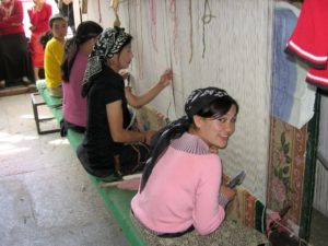 Uyghur women in the city of Hotan, East Turkistan making carpets in a carpet factory.